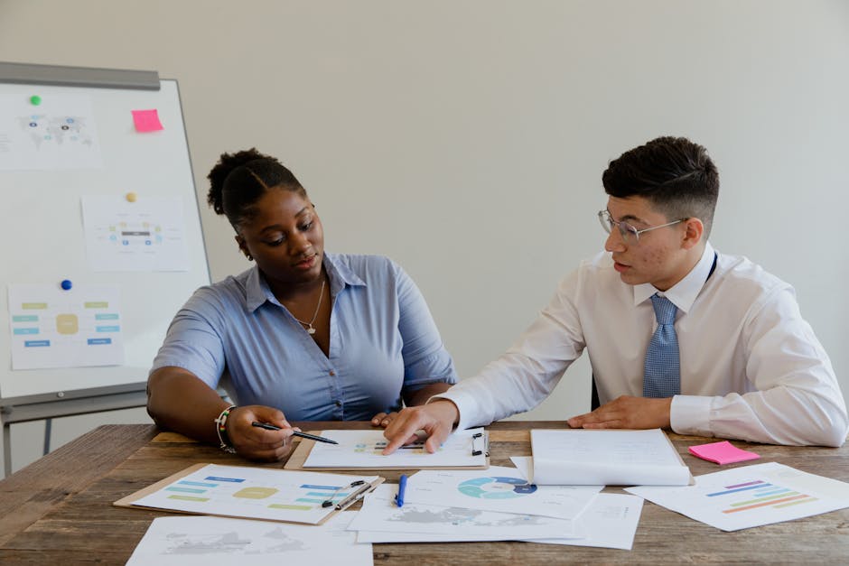 Diverse team of professionals engaged in an office discussion, analyzing charts and documents.